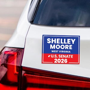 May include: A rectangular sticker with the text "SHELLEY MOORE WEST VIRGINIA U.S. SENATE 2026" in white on a blue and red background. The sticker is on the back of a white car.