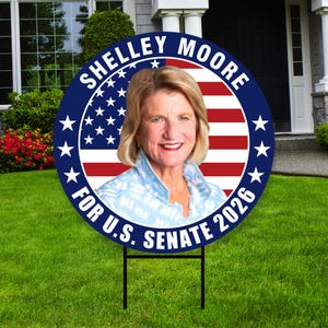May include: A circular political sign with a portrait of Shelley Moore. The sign has a blue border with white stars and the text "Shelley Moore For U.S. Senate 2026". The background features the American flag.