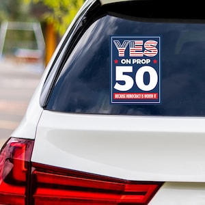 May include: A rectangular sticker on a car window with the text "YES ON PROP 50" in red, white, and blue. The number "50" is prominently displayed in white. The phrase "BECAUSE DEMOCRACY IS WORTH IT" is at the bottom.