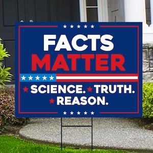 May include: A blue yard sign with the words "FACTS MATTER" in white and red. Below, it reads "SCIENCE. TRUTH. REASON." in white text with red stars. The sign is mounted on a metal frame.