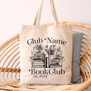 Puede incluir: Una bolsa de lona blanca con texto negro y un gr&aacute;fico de libros y plantas. El texto dice "Club Name Book Club est. 2024".