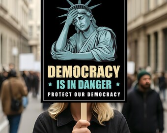 May include: A sign held by a person with the text "DEMOCRACY IS IN DANGER PROTECT OUR DEMOCRACY" and an illustration of the Statue of Liberty. The sign is black with white and yellow text and a black border. The Statue of Liberty is in shades of blue.
