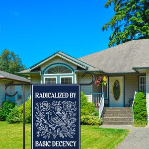 Puede incluir: Una bandera de jard&iacute;n azul marino con texto blanco y un dise&ntilde;o de p&aacute;jaro y flores. La bandera dice "RADICALIZED BY BASIC DECENCY". La bandera se muestra en un jard&iacute;n delantero con una casa y cielo azul en el fondo.