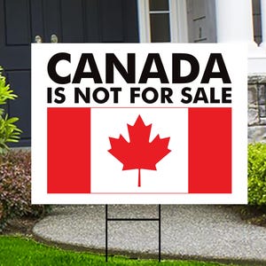 May include: A white sign with black text that reads "CANADA IS NOT FOR SALE". The sign features a red and white Canadian flag with a red maple leaf in the centre. The sign is displayed on a lawn with green grass.