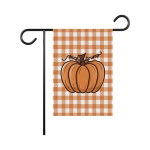 May include: A garden flag with a black metal stand. The flag features a pumpkin illustration with the words "fuck trump" in a script font. The background is a brown and white checkered pattern.