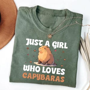 May include: Green t-shirt with a cartoon capybara and the text "Just a girl who loves capybaras".