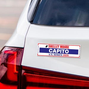May include: A rectangular bumper sticker with the text "SHELLEY MOORE CAPITO U.S. SENATE 2026" in red and white lettering on a blue background. The sticker is on the back of a white car.