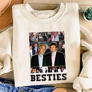 May include: Cream-colored sweatshirt featuring a collage of images and the word "BESTIES" in bold, black letters. The collage includes photos of two men. The sweatshirt is made of a soft material and has a crew neck.