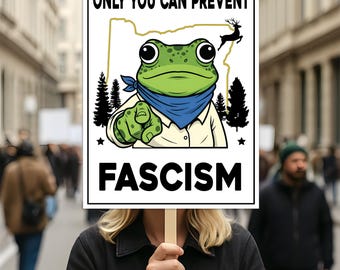 May include: A protest sign held by a person, featuring a cartoon frog with a blue bandana and the text "ONLY YOU CAN PREVENT FASCISM." The frog is pointing, with the Oregon state outline and a deer silhouette in the background.