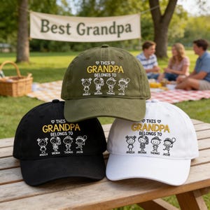 May include: Three baseball caps in olive green, black, and white. Each cap features embroidered text that reads THIS GRANDPA BELONGS TO above four stick figure illustrations of children labeled Angela, Brenda, Thomas, and Jacob in white thread.