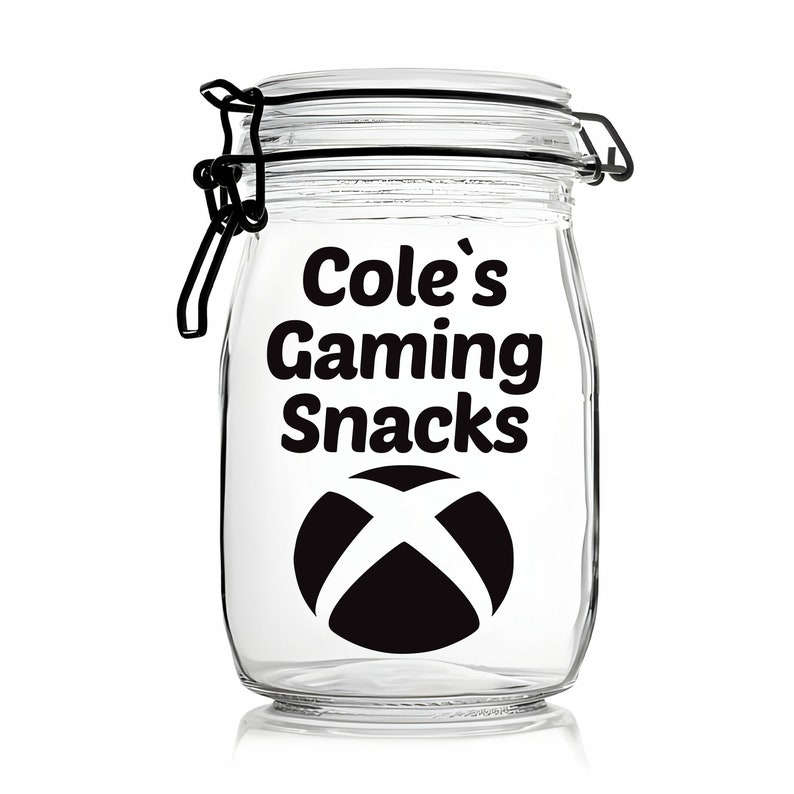 Peut inclure: Un pot en verre transparent avec un couvercle noir et une &eacute;tiquette noire qui dit "Cole's Gaming Snacks" avec un logo Xbox.