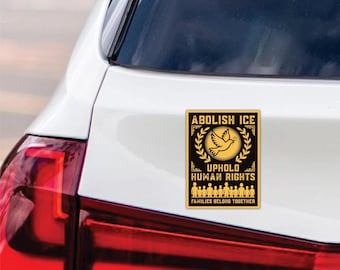 May include: A rectangular sticker with a black background and gold trim is affixed to a white car. The sticker reads "ABOLISH ICE" above a dove and olive branch design, with "UPHOLD HUMAN RIGHTS" and "FAMILIES BELONG TOGETHER" below.