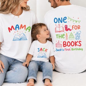 May include: Three white t-shirts featuring colorful graphics. One shirt says MAMA with a book, one says JACK with a book, and one says ONE FOR THE BOOKS with a book, worm, candle, cake, bear, and the text Jack's First Birthday in various colors.