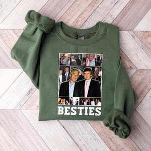 May include: Green sweatshirt with a collage of photos and the word "BESTIES" in white. The collage features two men in suits. The sweatshirt is made of a soft material and has long sleeves.