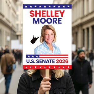 May include: A sign held by a person with the words "Shelley Moore" in red and blue, and "U.S. Senate 2026" in white and red. The sign features a photo of a woman and a silhouette of West Virginia.