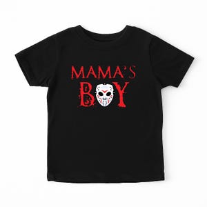 May include: Black t-shirt with the words "MAMA'S BOY" in red, distressed font. A white hockey mask with red and blue details is centered below the text. The shirt is a short-sleeved crew neck.