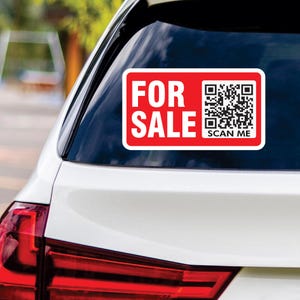 May include: Red and white sticker with the text "FOR SALE" and a black and white QR code with the text "SCAN ME" below it. The sticker is on the back window of a white car.