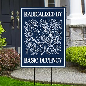 May include: A navy blue yard sign with white text and a floral bird design. The sign reads "RADICALIZED BY BASIC DECENCY". The bird is perched on a branch surrounded by flowers and leaves.