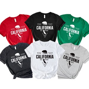 May include: Six t-shirts in different colors with a black and white graphic design of a bear and the text "CALIFORNIA Est. 1850" in a triangle shape.