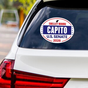 May include: Oval car sticker with the text "SHELLEY MOORE CAPITO U.S. SENATE 2026." The sticker has a white background with a red and blue border. The text "CAPITO" is in large, bold, white letters on a blue background.