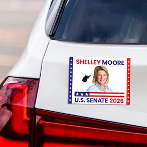 May include: A rectangular bumper sticker with the text "SHELLEY MOORE" in red letters. The sticker features a portrait of a woman, a silhouette of West Virginia, and the text "U.S. SENATE 2026". The sticker is affixed to a white car.