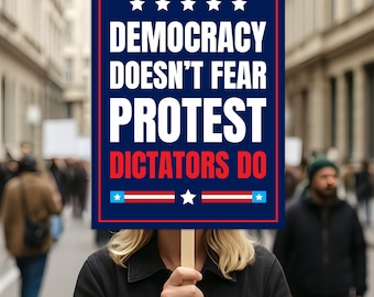 May include: A sign with the text "DEMOCRACY DOESN'T FEAR PROTEST DICTATORS DO" in white on a blue background, with red and white accents and stars. The sign is held by a person in front of a blurred crowd of people.