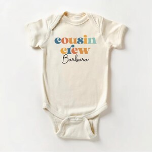 May include: A white baby onesie with the text "cousin crew Barbara" in colorful letters.