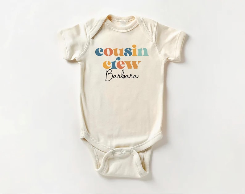 May include: A white baby onesie with the text "cousin crew Barbara" in colorful letters.