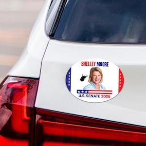 May include: An oval car sticker with the text "Shelley Moore U.S. Senate 2026." The sticker features a portrait of Shelley Moore, the outline of West Virginia, and blue and red accents. It is affixed to a white car.