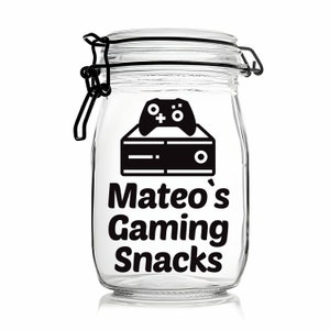 Peut inclure: Un pot en verre transparent avec un autocollant noir et blanc qui dit "Mateo's Gaming Snacks". L'autocollant repr&eacute;sente &eacute;galement une manette de jeu vid&eacute;o et une console.