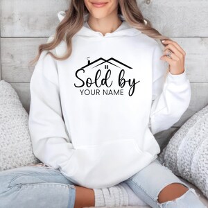 May include: White hooded sweatshirt with a black graphic of a house with the text "Sold by YOUR NAME" printed on the front.