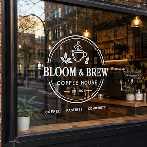 May include: A white vinyl window decal featuring a circular logo with a coffee cup icon, the text BLOOM & BREW COFFEE HOUSE EST. 2021, and the words COFFEE, PASTRIES, COMMUNITY displayed on a glass storefront window with a view of a cafe interior.