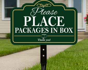 May include: A dark green sign with gold trim and white text that reads "Please PLACE PACKAGES IN BOX". The sign is mounted on a black metal post and is placed in a grassy yard.