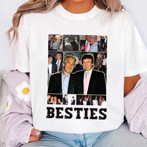 May include: White t-shirt featuring a collage of photographs and the word "BESTIES" in black. The collage includes images of two men in suits, with a pink tie. The shirt is a casual style.