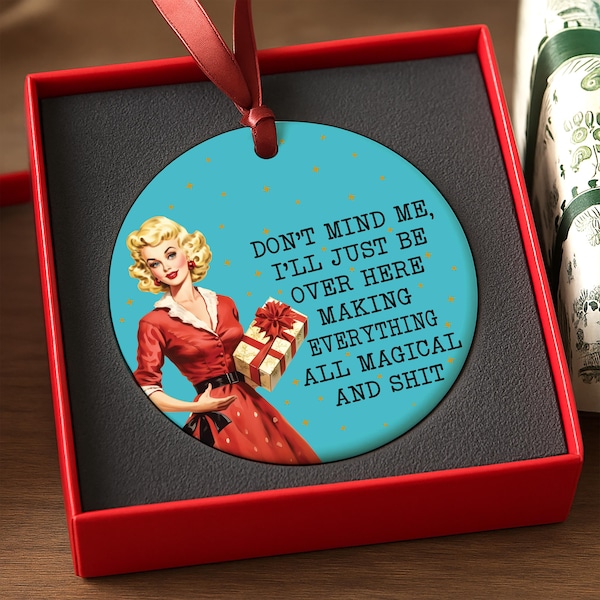 May include: A teal circular ornament featuring a retro illustration of a woman in a red dress holding a gift. The ornament has the text "DON'T MIND ME, I'LL JUST BE OVER HERE MAKING EVERYTHING ALL MAGICAL AND SHIT."
