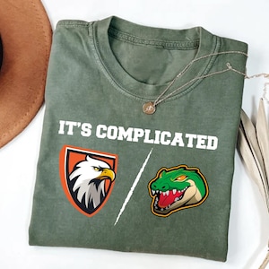 May include: A green t-shirt with the text "It's complicated" printed on it. The shirt features a graphic of an eagle and an alligator.