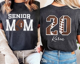 May include: Dark gray t-shirts with football-themed designs. One shirt features "SENIOR MOM" with a football graphic and the number "26". The other shirt displays the number "20" with a football design and the name "Karen".