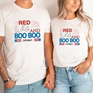 May include: Two white t-shirts with red, white, and blue text and graphics. The text on the shirts reads "Red White and Boo Boo Crew".