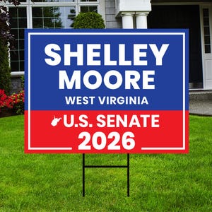May include: A blue and red political campaign sign on a lawn. The sign reads "Shelley Moore, West Virginia, U.S. Senate 2026" in white text. The sign is supported by a black metal stake.