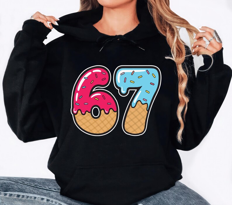 May include: Black hooded sweatshirt with a colorful graphic of the number 67. The number 6 is designed as a pink donut with sprinkles, and the number 7 is blue with sprinkles, resembling melting ice cream. The sweatshirt is made of a soft material.