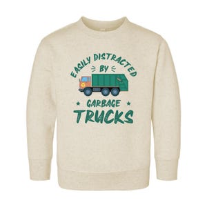 May include: A beige sweatshirt with a green graphic of a refuse truck and the text "Easily Distracted By Garbage Trucks".