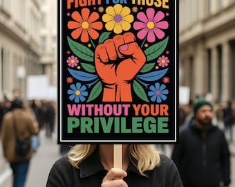 May include: A protest sign with the text "FIGHT FOR THOSE WITHOUT YOUR PRIVILEGE". The sign features a raised orange fist, surrounded by flowers in orange, yellow, and pink. The background is a blurred street scene with people walking in a city.