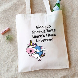 May include: White tote bag with a unicorn and a cat riding on its back. The bag has the text "Giddy up Sparkle Farts there's Chaos to Spread" printed on it.