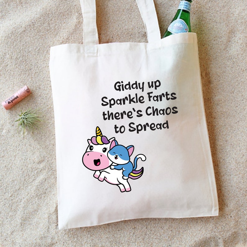 May include: White tote bag with a unicorn and a cat riding on its back. The bag has the text "Giddy up Sparkle Farts there's Chaos to Spread" printed on it.