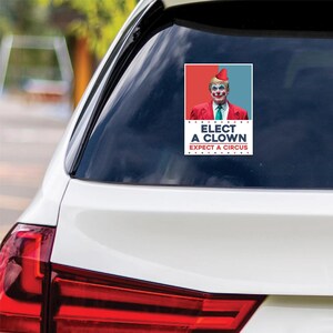May include: A white car with a sticker on the back window. The sticker features a person wearing a clown makeup and a red hat. The text on the sticker reads "Elect a Clown Expect a Circus".