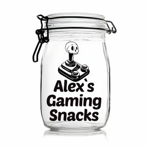 Peut inclure: Un pot en verre transparent avec un couvercle noir et un autocollant noir et blanc. L'autocollant repr&eacute;sente un joystick avec un cr&acirc;ne et des os crois&eacute;s et le texte "Alex's Gaming Snacks".