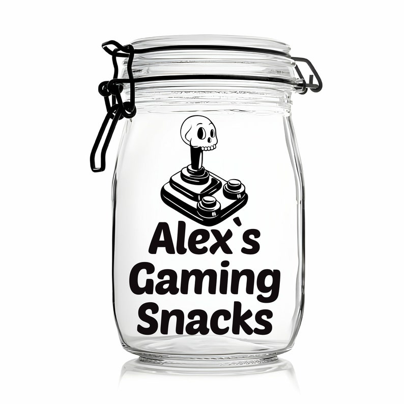 Peut inclure: Un pot en verre transparent avec un couvercle noir et un autocollant noir et blanc. L'autocollant repr&eacute;sente un joystick avec un cr&acirc;ne et des os crois&eacute;s et le texte "Alex's Gaming Snacks".
