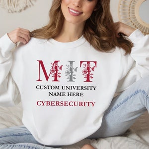 May include: White sweatshirt with the letters MIT in red and gray with floral accents. The text "Custom University Name Here Cybersecurity" is printed below the letters.