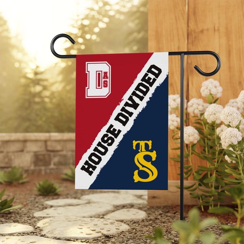 K&ouml;nnte beinhalten: Eine rot-blaue Gartenflagge mit dem Text "House Divided" und den Buchstaben "D.A.S." und "T.S." in Wei&szlig; und Gelb.