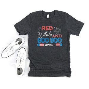 May include: Dark gray t-shirt with the text "Red White and Boo Boo crew" in red, white, and blue. The text is surrounded by fireworks.